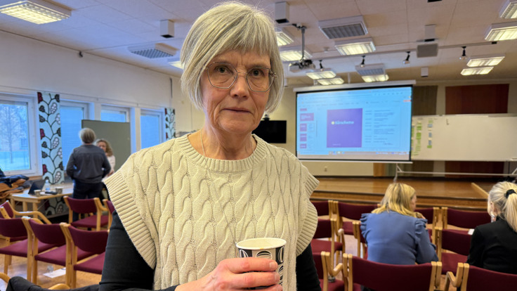 En kvinna som håller en kopp i ett rum fullt av människor.