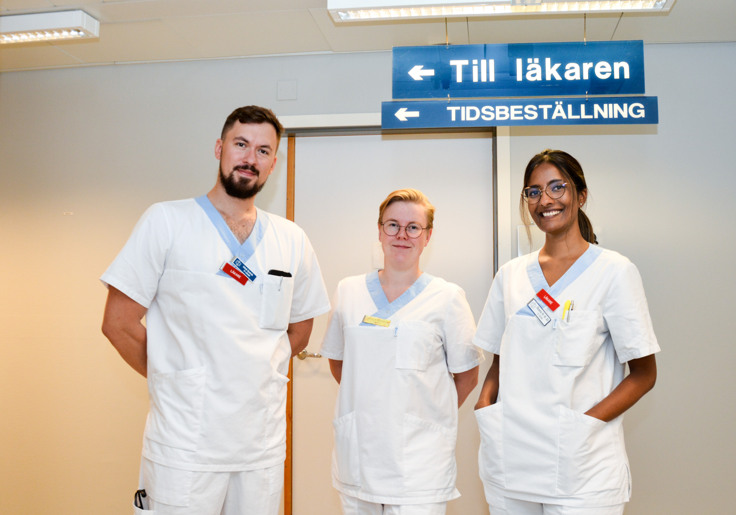 Jakub, Jenny och Shanie i arbetskläder inne på hälsocentralen.