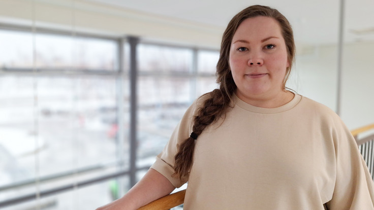 En kvinna i en beige skjorta st&aring;r p&aring; en balkong.
