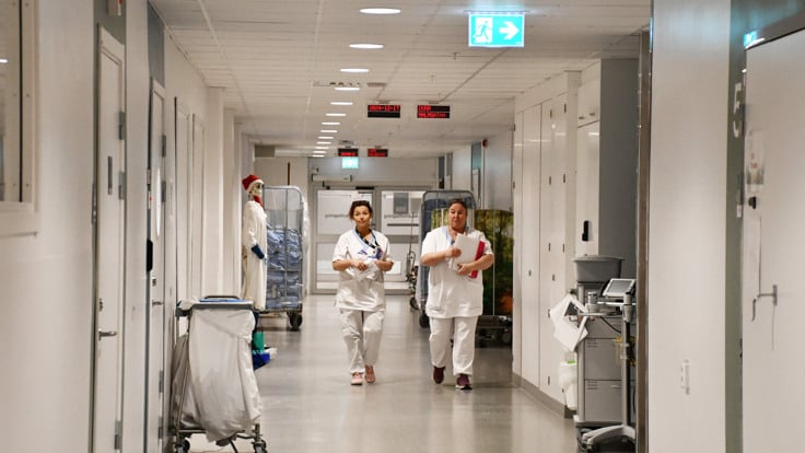 Tv&aring; sjuksk&ouml;terskor som g&aring;r l&auml;ngs en sjukhuskorridor.