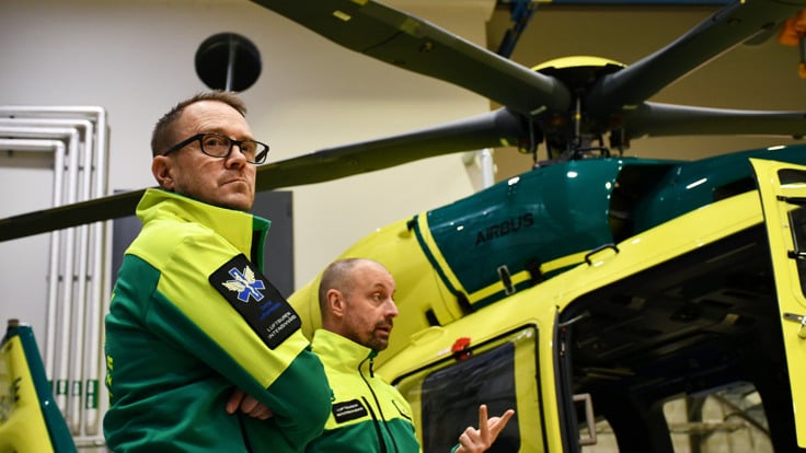 Tv&aring; m&auml;n som st&aring;r framf&ouml;r en helikopter.