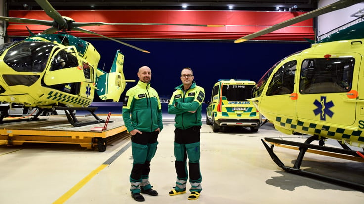 Tv&aring; ambulanssjukv&aring;rdare som st&aring;r framf&ouml;r en helikopter.