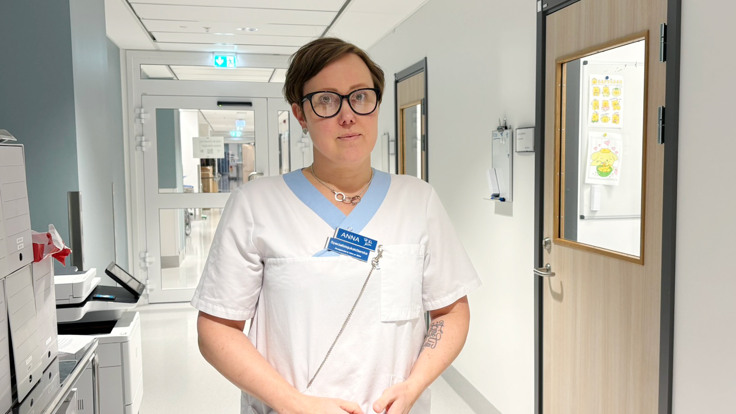 En kvinna i sjukhuskl&auml;der st&aring;r i en korridor.
