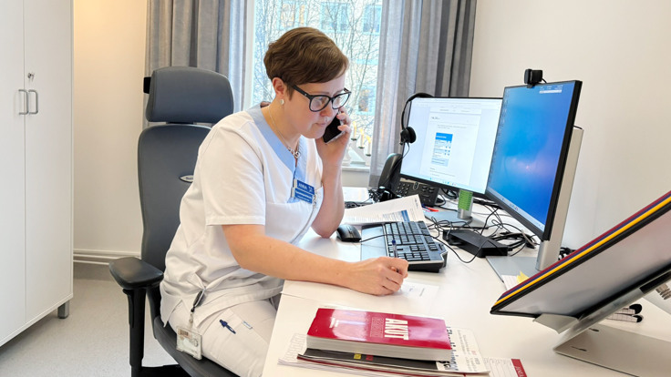 En kvinna sitter vid ett skrivbord och pratar i mobiltelefon.
