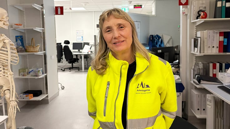 En kvinna i gul jacka st&aring;r i ett kontor.