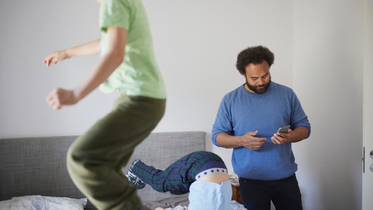 En tittar i sin telefon medan barn leker runt honom.