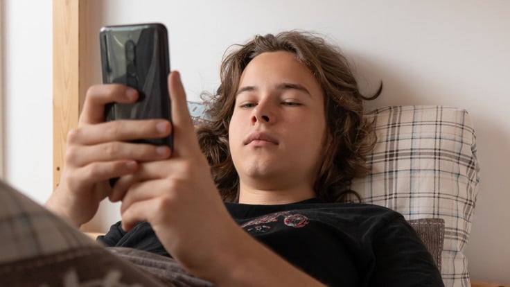 En man som ligger i s&auml;ngen och h&aring;ller i en mobiltelefon.