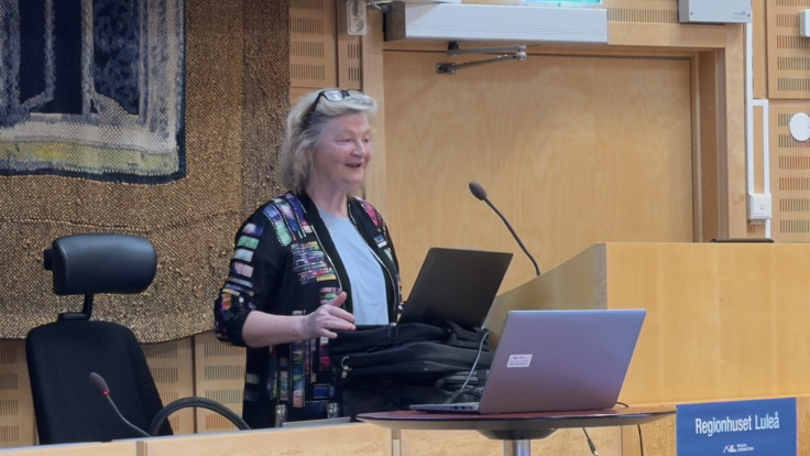 En kvinna st&aring;r vid ett podium med en b&auml;rbar dator framf&ouml;r sig.