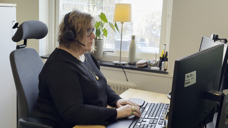 En kvinna sitter vid ett skrivbord och anv&auml;nder en dator.