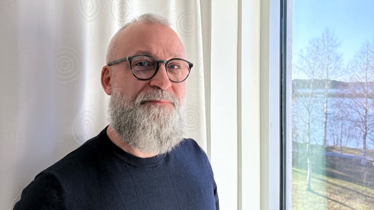 En man med skägg och glasögon som står framför ett fönster.