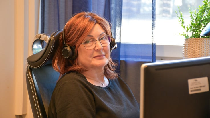 En kvinna med h&ouml;rlurar sitter framf&ouml;r en dator.
