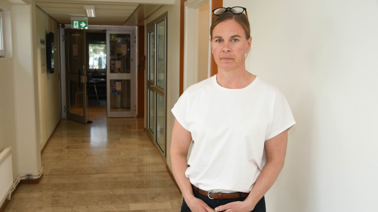 En kvinna som st&aring;r i en hall med h&auml;nderna i fickorna.