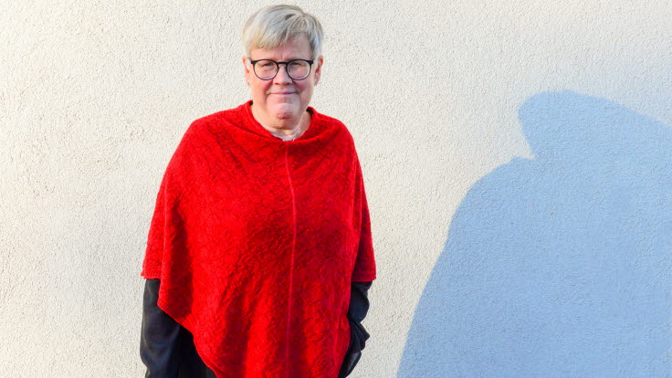 Kvinna klädd i rött framför en vit vägg.