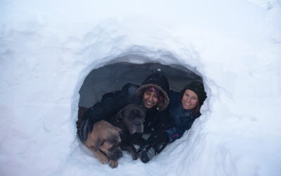 Två glada kvinnor och två hundar i en snögrotta.