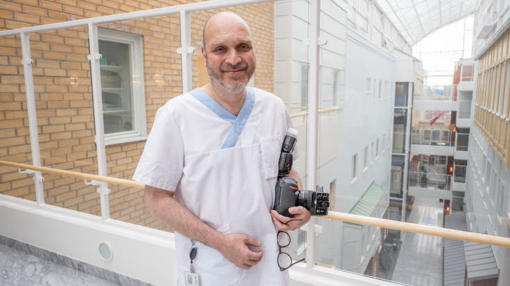 Sjukhusfotografen Bert-Ola Isaksson i vita arbetskläder med en kamera i handen.