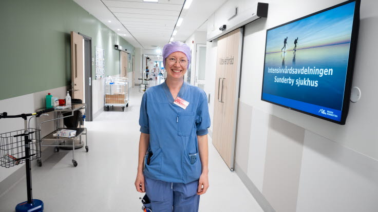 Kvinna i blå arbetskläder i en sjukhuskorridor.