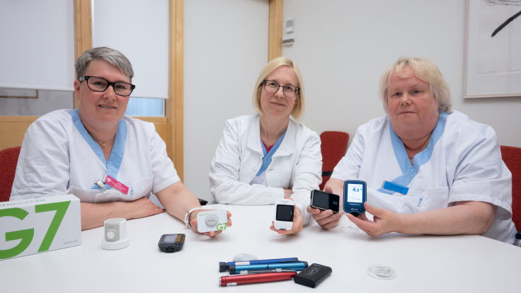 Tre diabetessköterskor sitter vid ett bord med tekniska diabeteshjälpmedel framför sig.