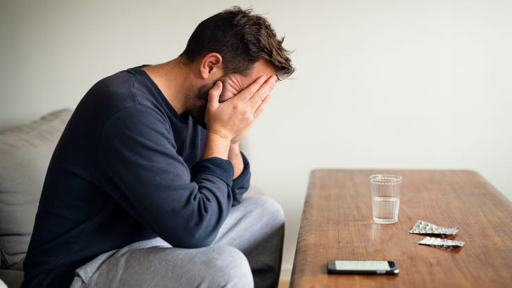 Man sitter i en soffa med huvudet i händerna.  Framför honom på bordet ligger en telefon och två kartor med tabletter.