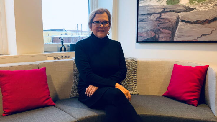 Elisabeth Lindblad sitter i en soffa med röda kuddar.