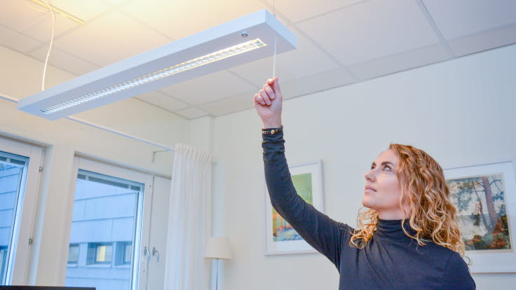 Underhållsingenjören Annica, klädd i svart tröja, drar i en snodd i en LED-taklampa.